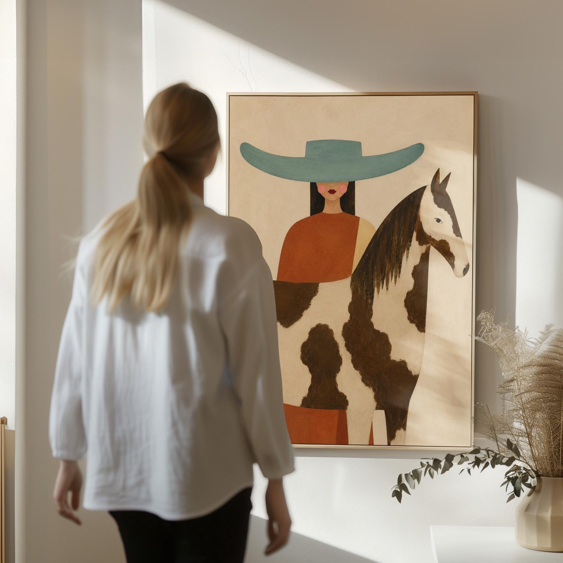 Woman in a teal hat beside a brown and white pinto horse in warm light, canvas print presented in a light, minimal room