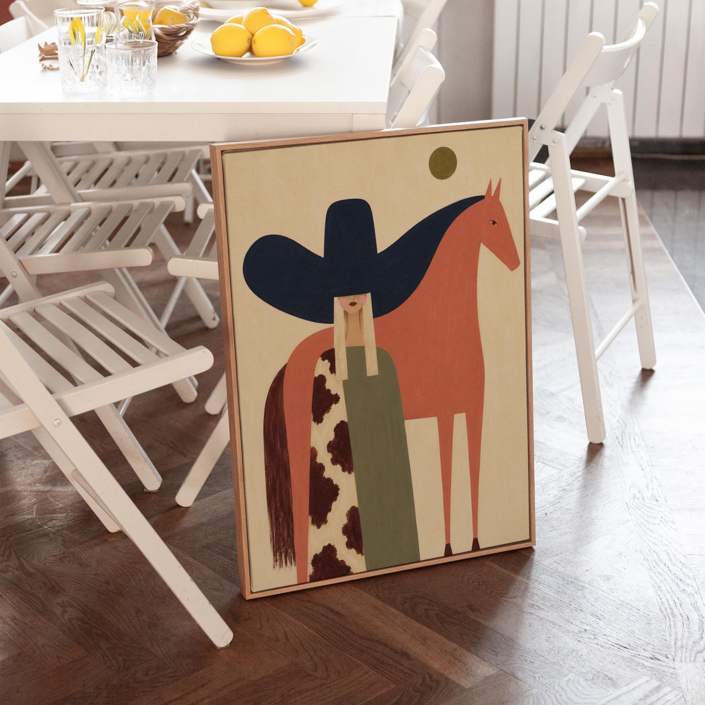 Cowgirl in a black sombrero and cow print cape beside a rust red horse, canvas print shown in a sunlit, contemporary room