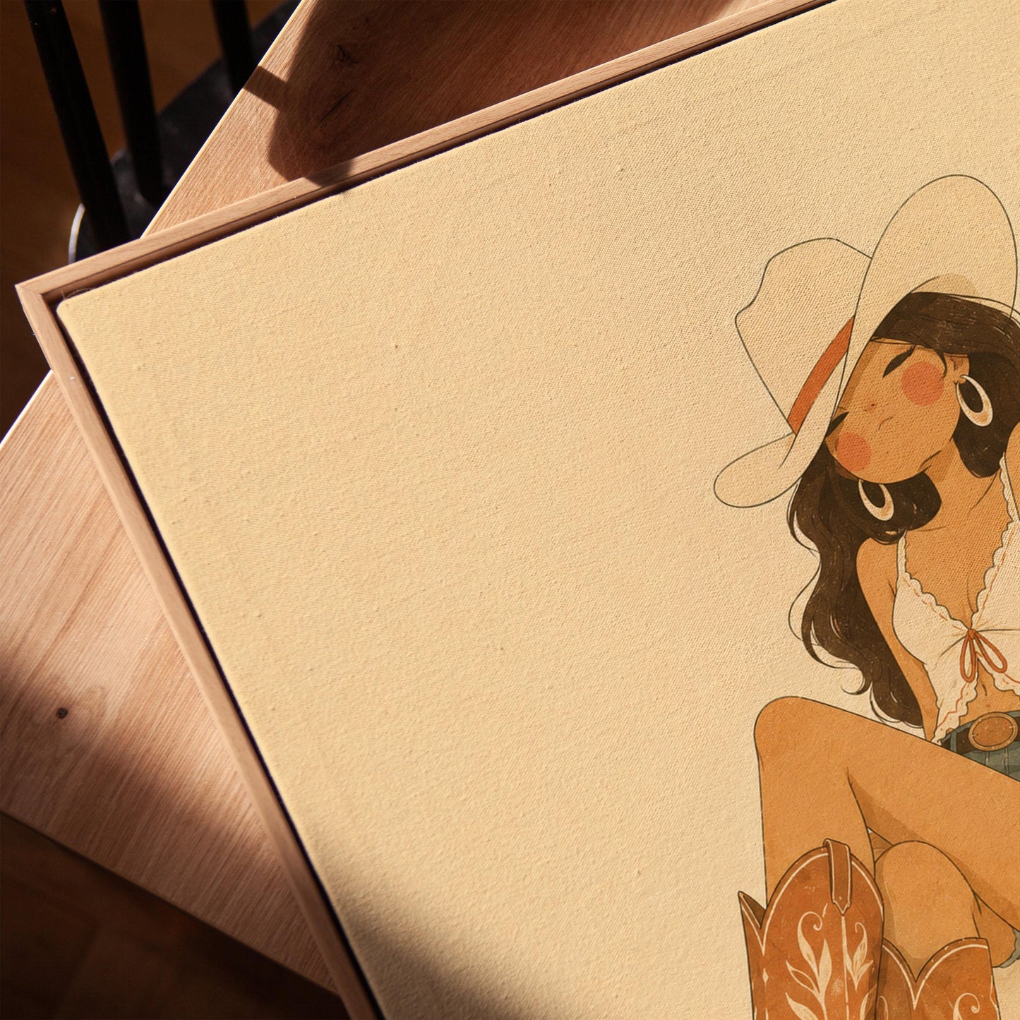 Cowgirl in denim shorts and cowboy boots leaning back under a wide pale hat, canvas print in a warm, minimally styled interior