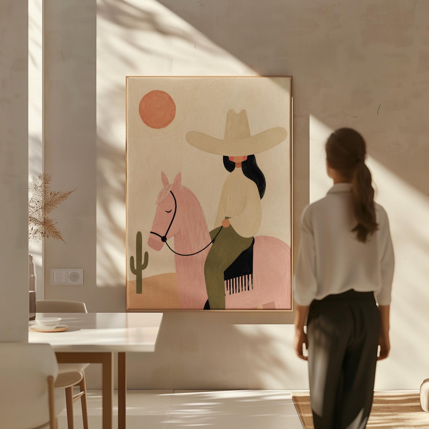 Cowgirl in a pale hat riding a soft pink horse past a desert cactus, canvas print displayed on a neutral wall in a styled interior