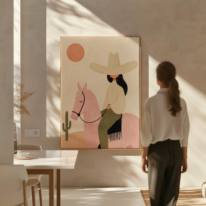 Cowgirl in a pale hat riding a soft pink horse past a desert cactus, canvas print displayed on a neutral wall in a styled interior