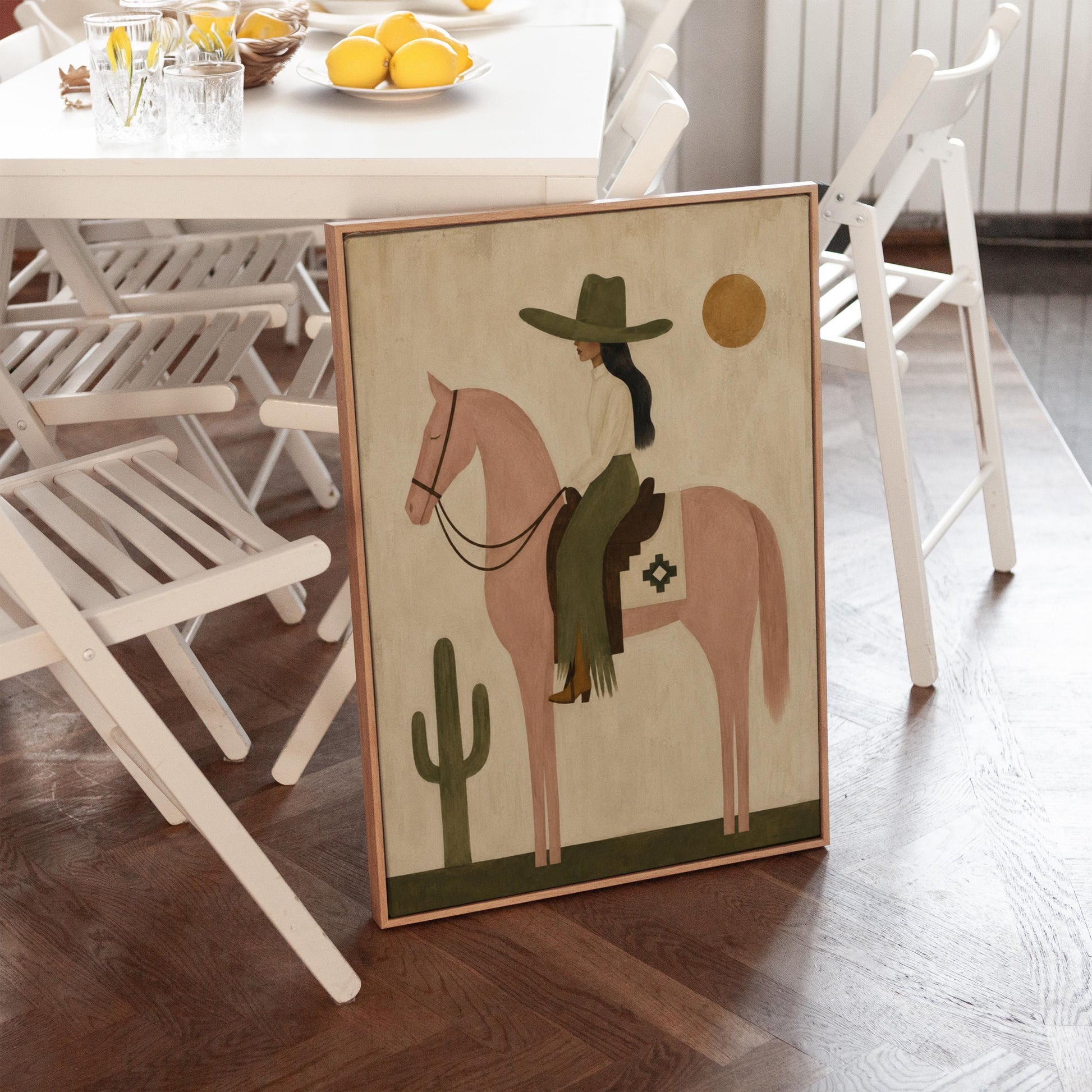 Cowgirl on a dusty pink horse beside a tall saguaro cactus, canvas print seen in a warm interior with natural light