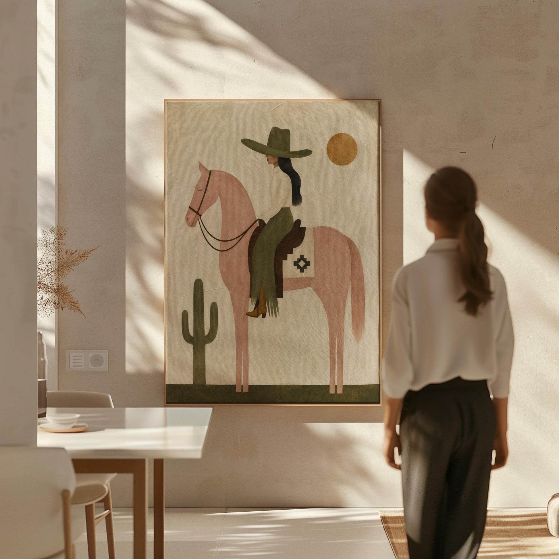 Cowgirl on a dusty pink horse beside a tall saguaro cactus, canvas wall art presented in a light, minimal room
