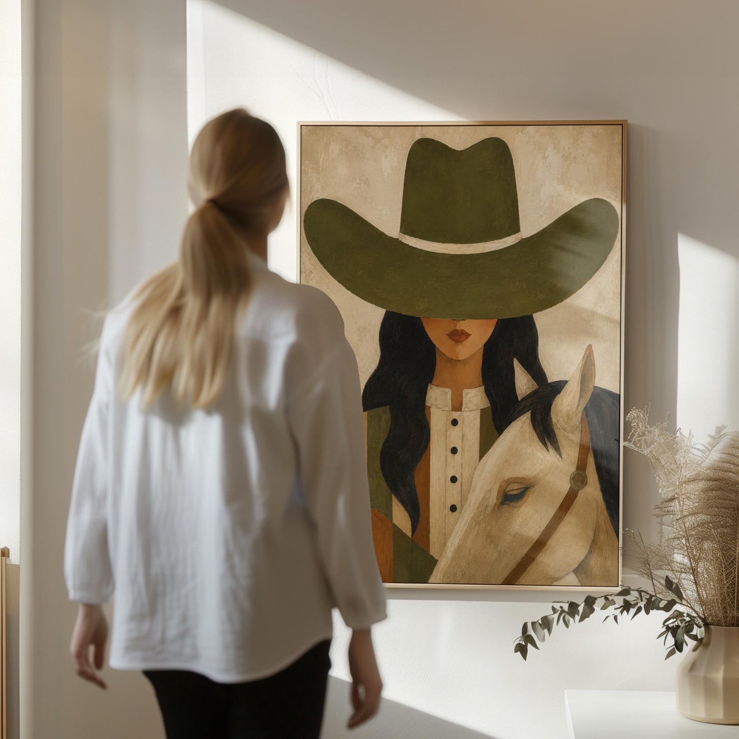 Cowgirl in an olive hat leaning close to a pale white horse, canvas wall art hanging in a calm, modern living space