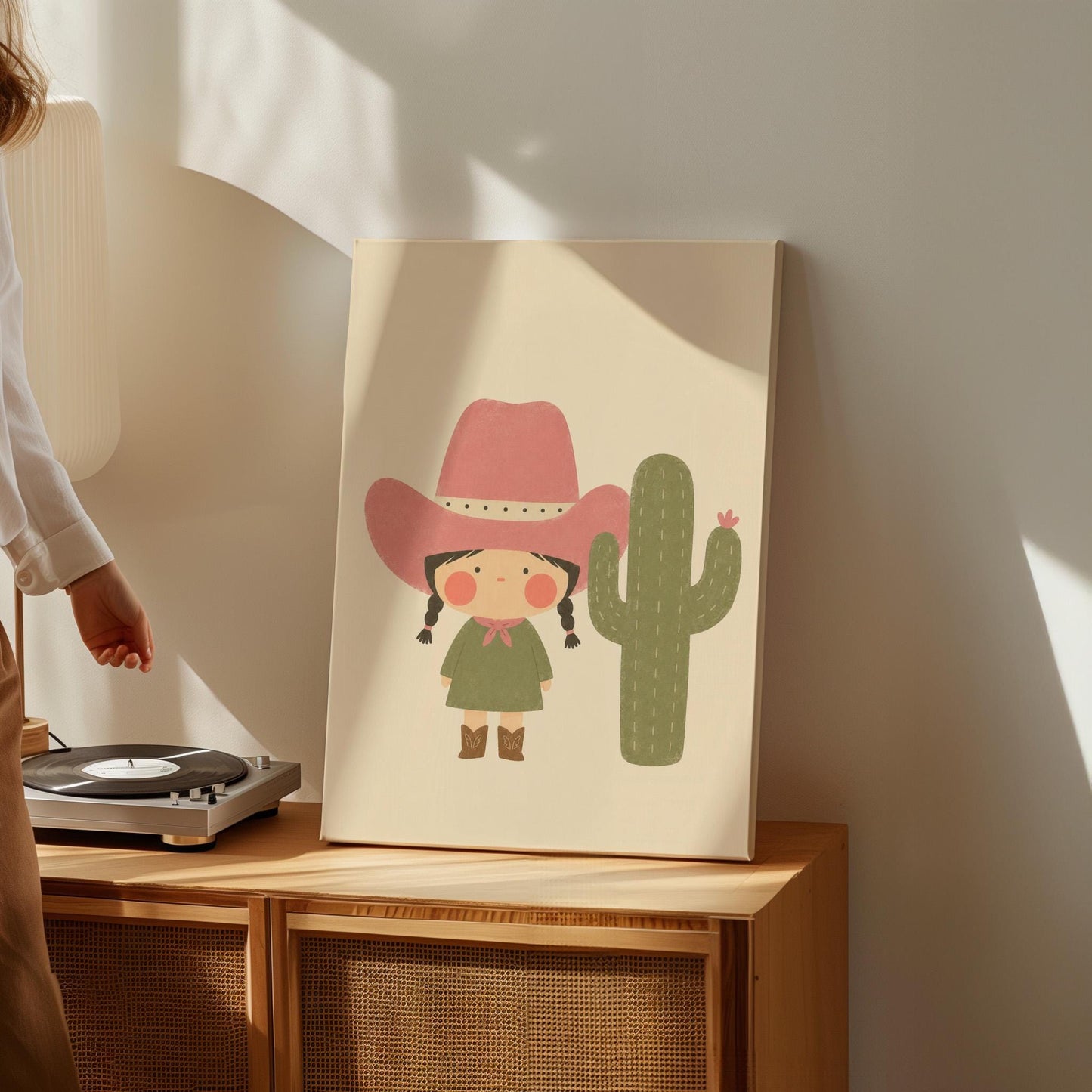 Little cowgirl in a pink hat next to a tall flowering cactus, canvas wall art presented in a light, minimal room
