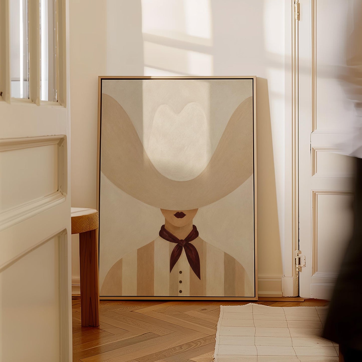 Woman under an oversized pale cowboy hat with a plum neckerchief, canvas wall art presented in a light, minimal room