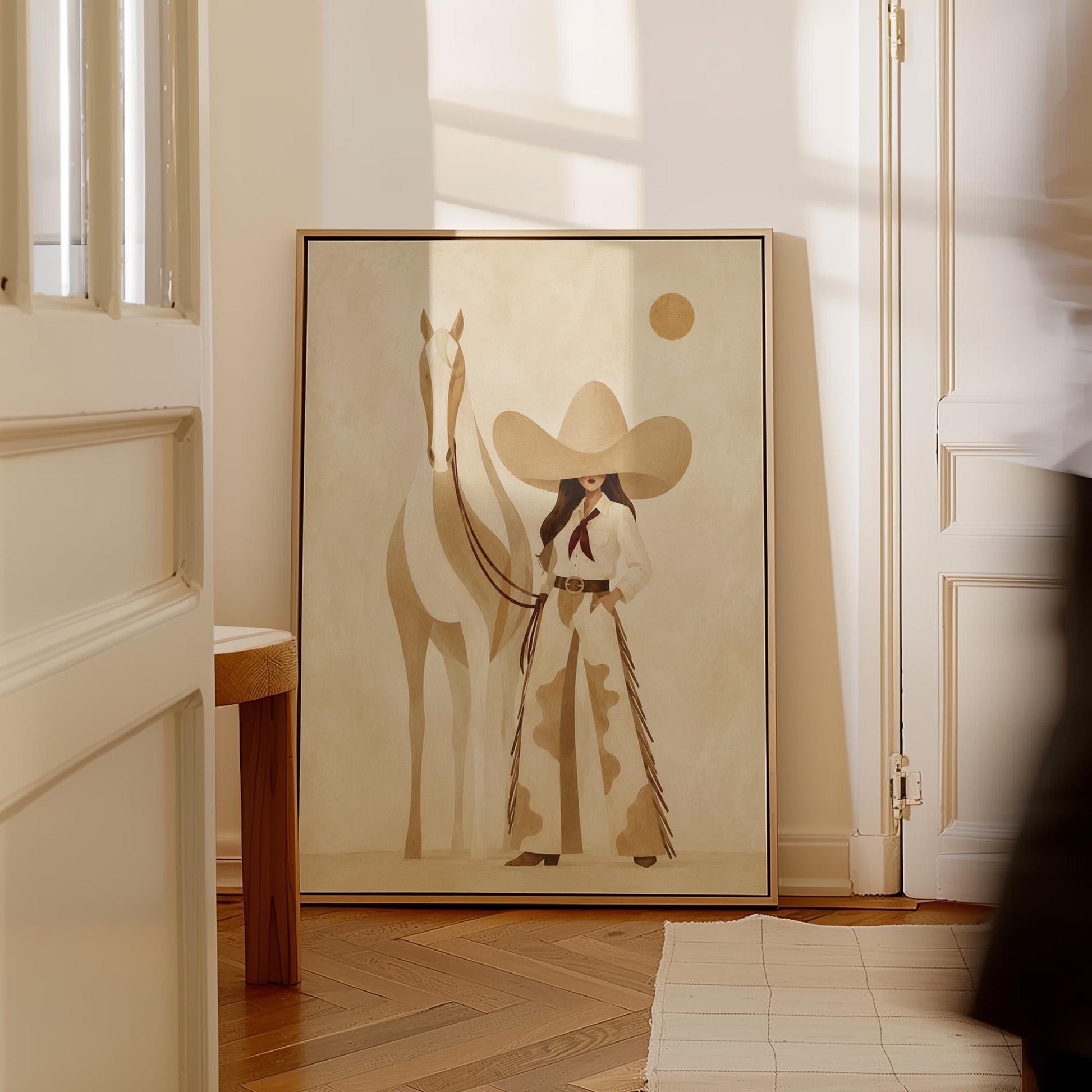 Cowgirl in cream chaps beside a pale horse under a small ochre sun, canvas print displayed on a neutral wall in a styled interior