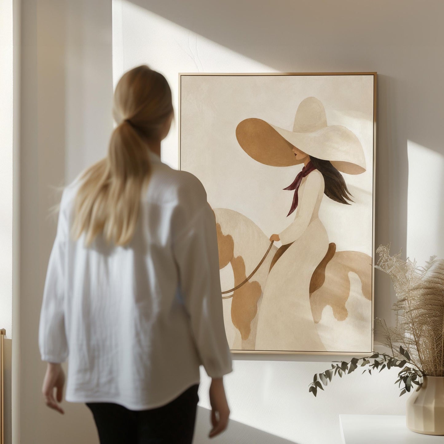Woman in a long white dress and floppy hat riding a spotted horse, canvas wall art styled against a soft white wall