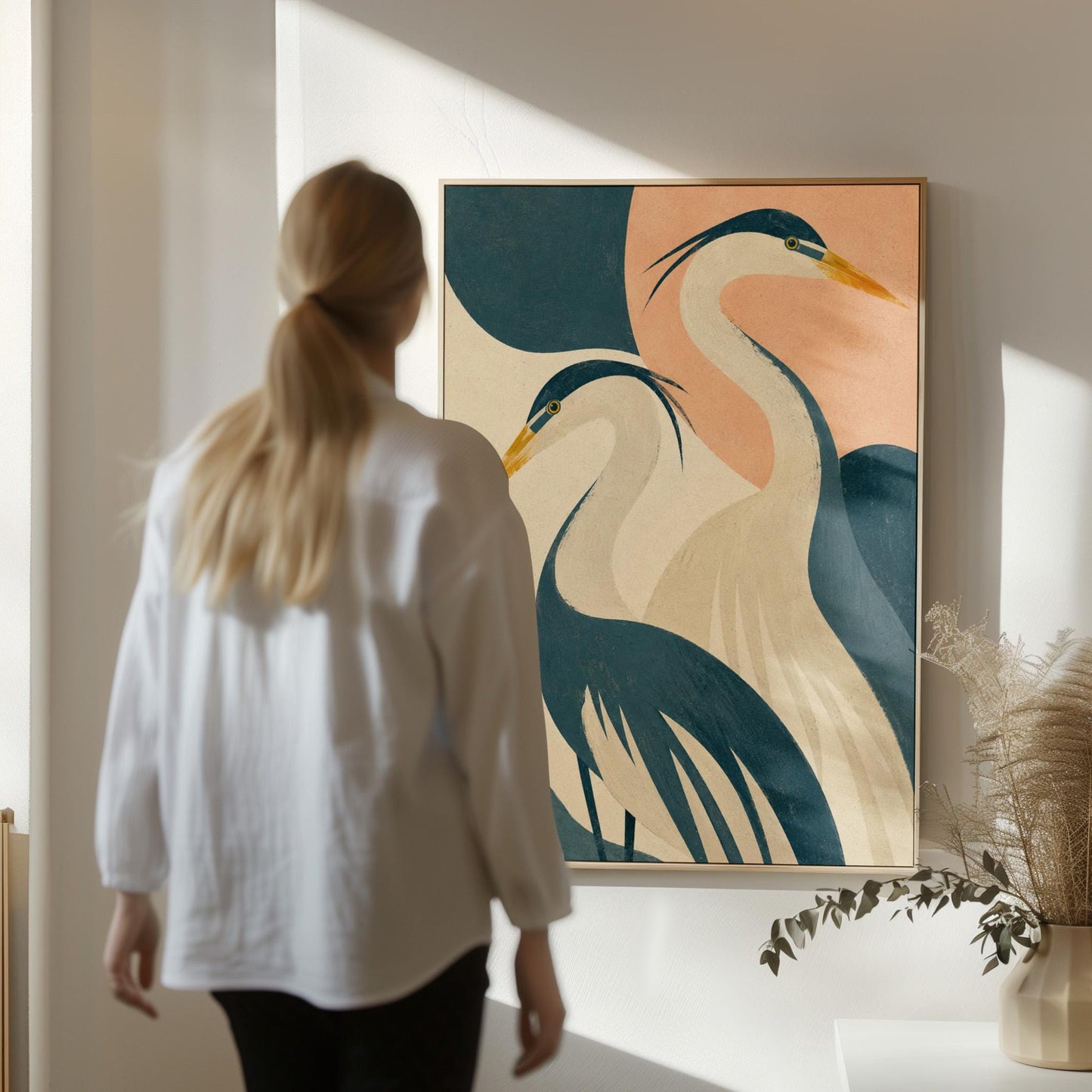 Two great herons with yellow beaks against a peach and teal sky, canvas print presented in a light, minimal room