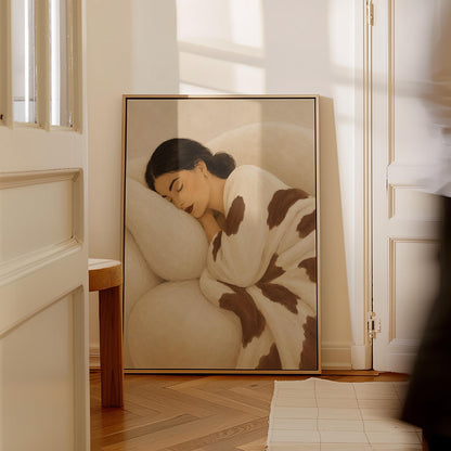Woman asleep on a pillow under a cream blanket with brown markings, canvas wall art presented in a light, minimal room