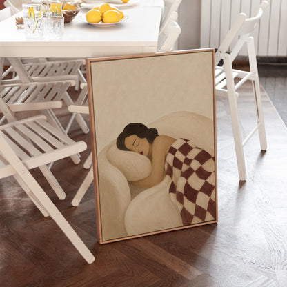 Woman sleeping under a burgundy and cream checkerboard blanket, canvas wall art styled against a soft white wall