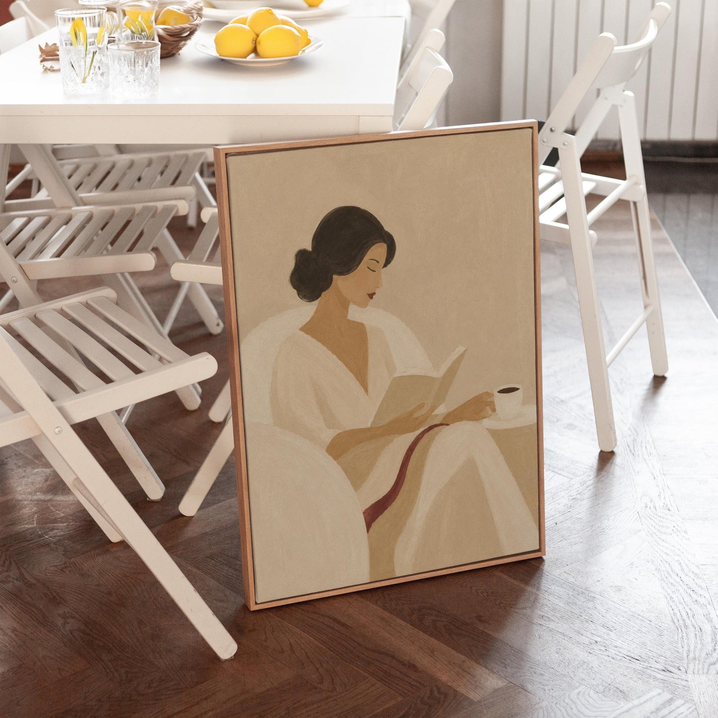 Woman in a white robe reading in an armchair with a black coffee, canvas wall art styled against a soft white wall
