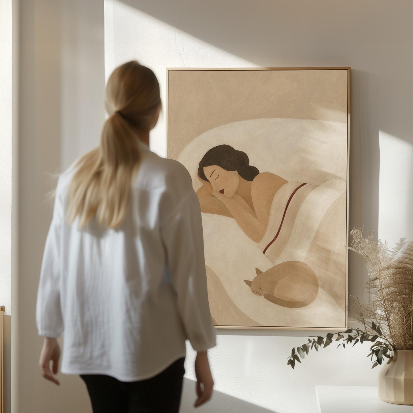 Woman sleeping with a small white cat curled at the foot of the bed, canvas wall art hanging in a calm, modern living space
