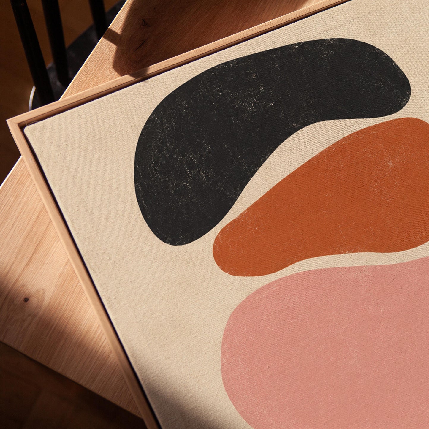 Five stacked pebble shapes in charcoal rust and blush on cream, canvas print in a warm, minimally styled interior