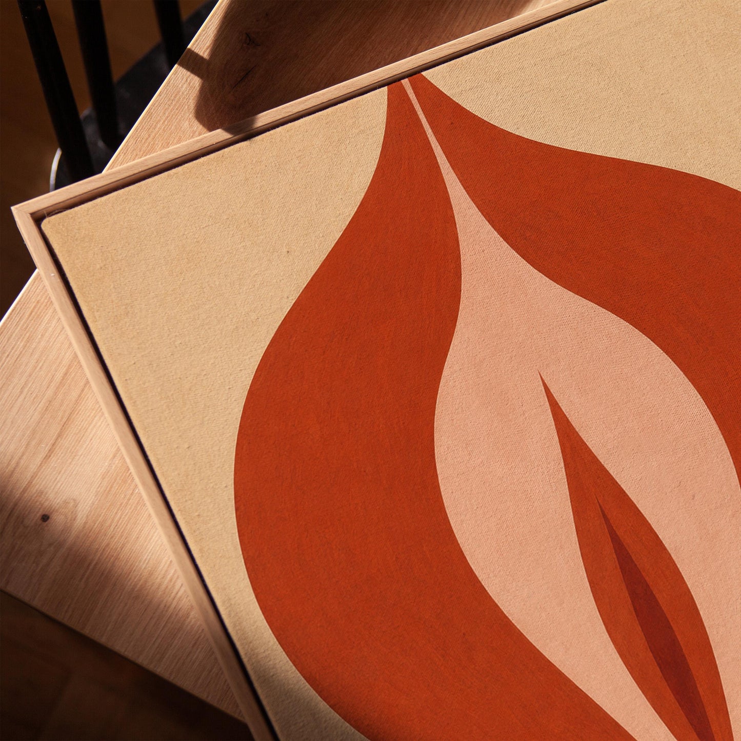 Rust red flame shaped form opening into blush and grey on sand, canvas print in a warm, minimally styled interior