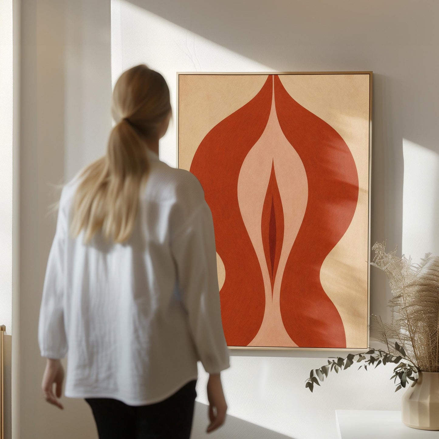 Rust red flame shaped form opening into blush and grey on sand, canvas print shown in a sunlit, contemporary room