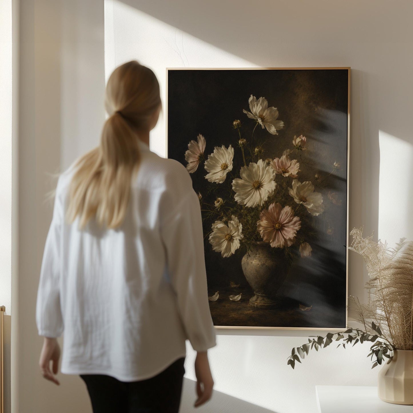 White cosmos flowers in a weathered stone vase, canvas wall art on a quiet wall in a considered interior