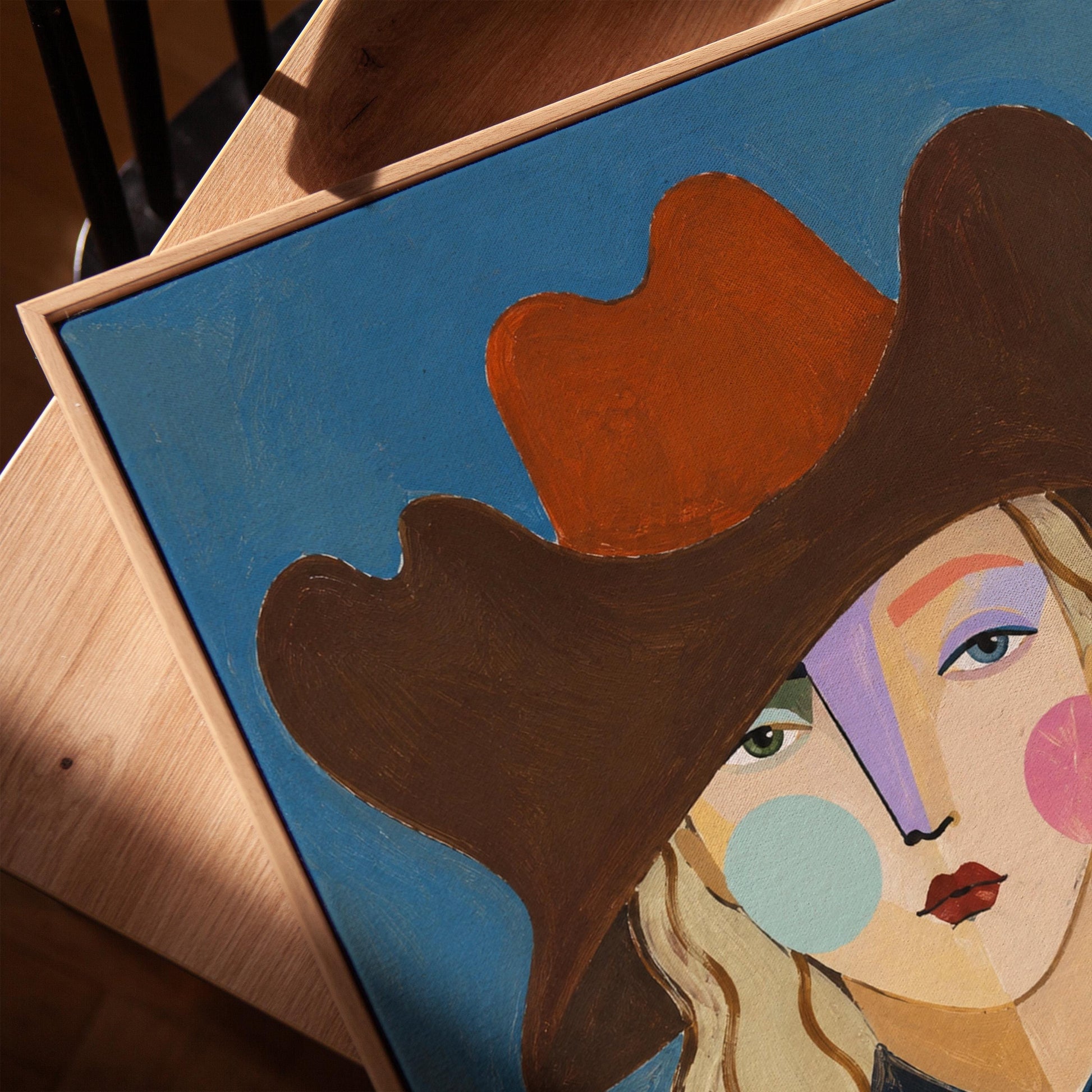 Blonde cowgirl in a rust cowboy hat with a cubist face on deep blue, canvas print in a warm, minimally styled interior