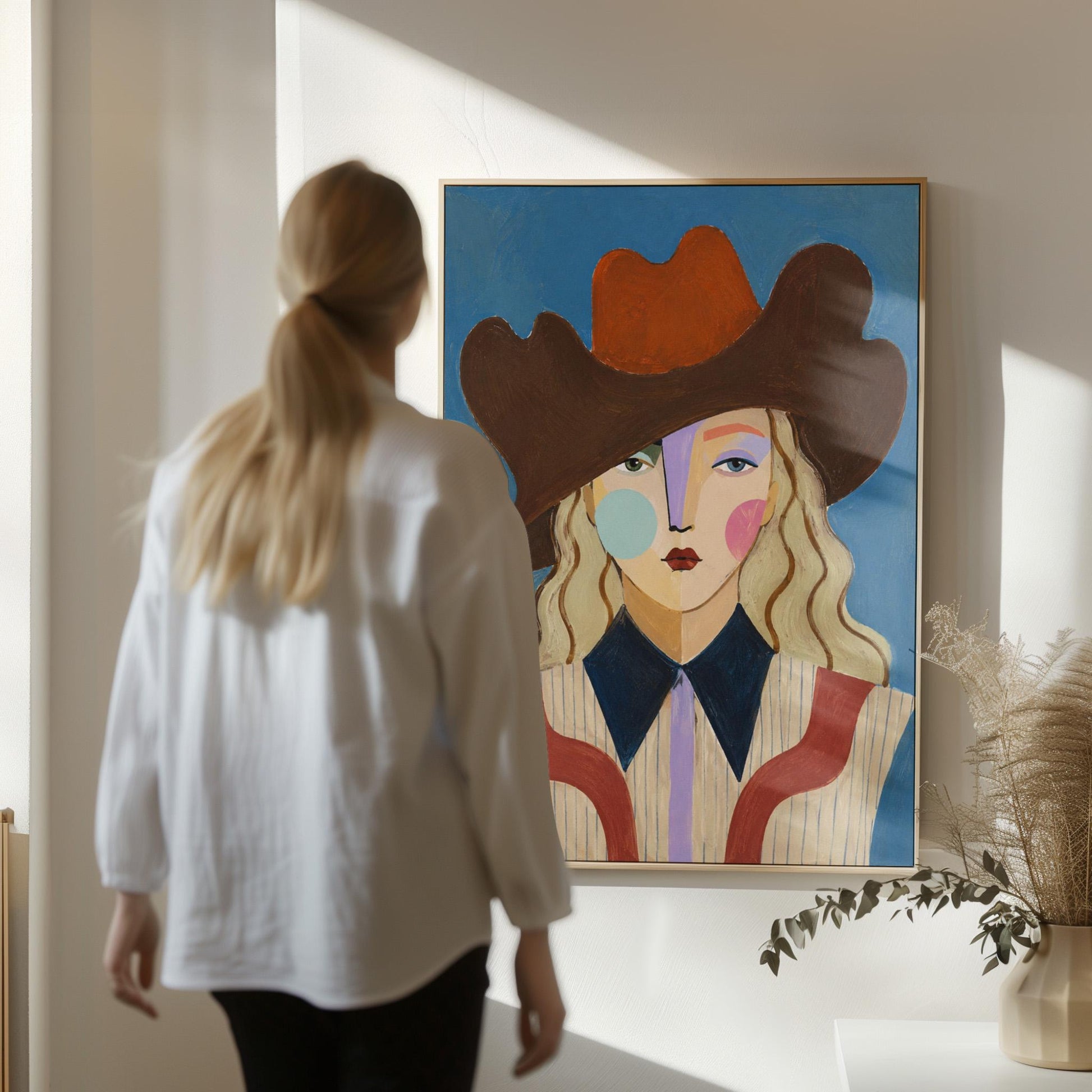 Blonde cowgirl in a rust cowboy hat with a cubist face on deep blue, canvas wall art seen in a warm interior with natural light