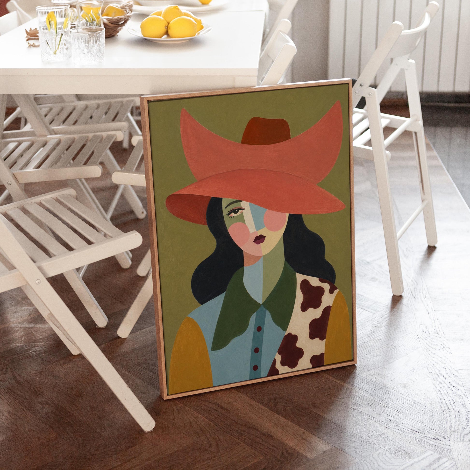 Cowgirl in a wide coral hat with a cubist face and cow-print collar on olive, canvas print displayed on a neutral wall in a styled interior