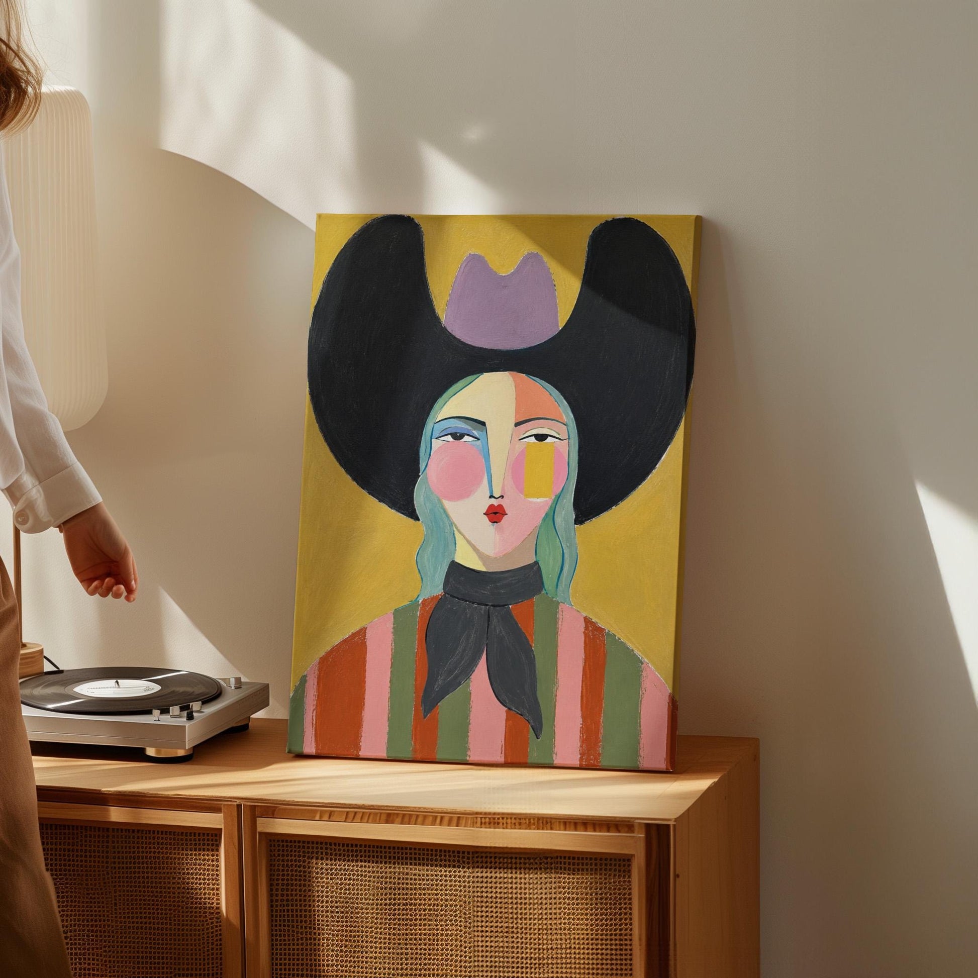 Folk cowgirl with teal hair, a big black hat and striped shirt on golden yellow, canvas wall art on a quiet wall in a considered interior