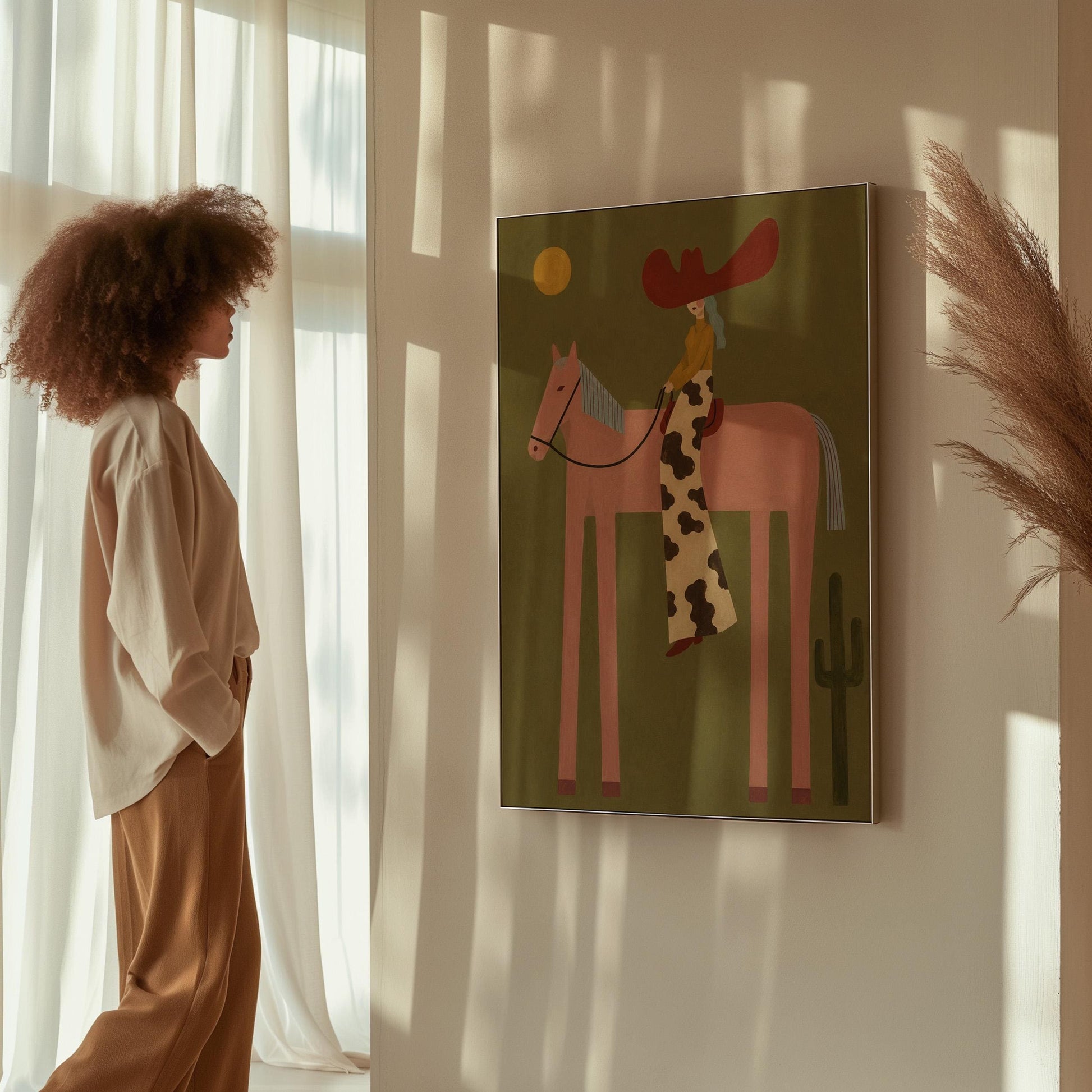 Cowgirl in a red hat riding a long-legged pink horse past a cactus at sunset, canvas print displayed on a neutral wall in a styled interior