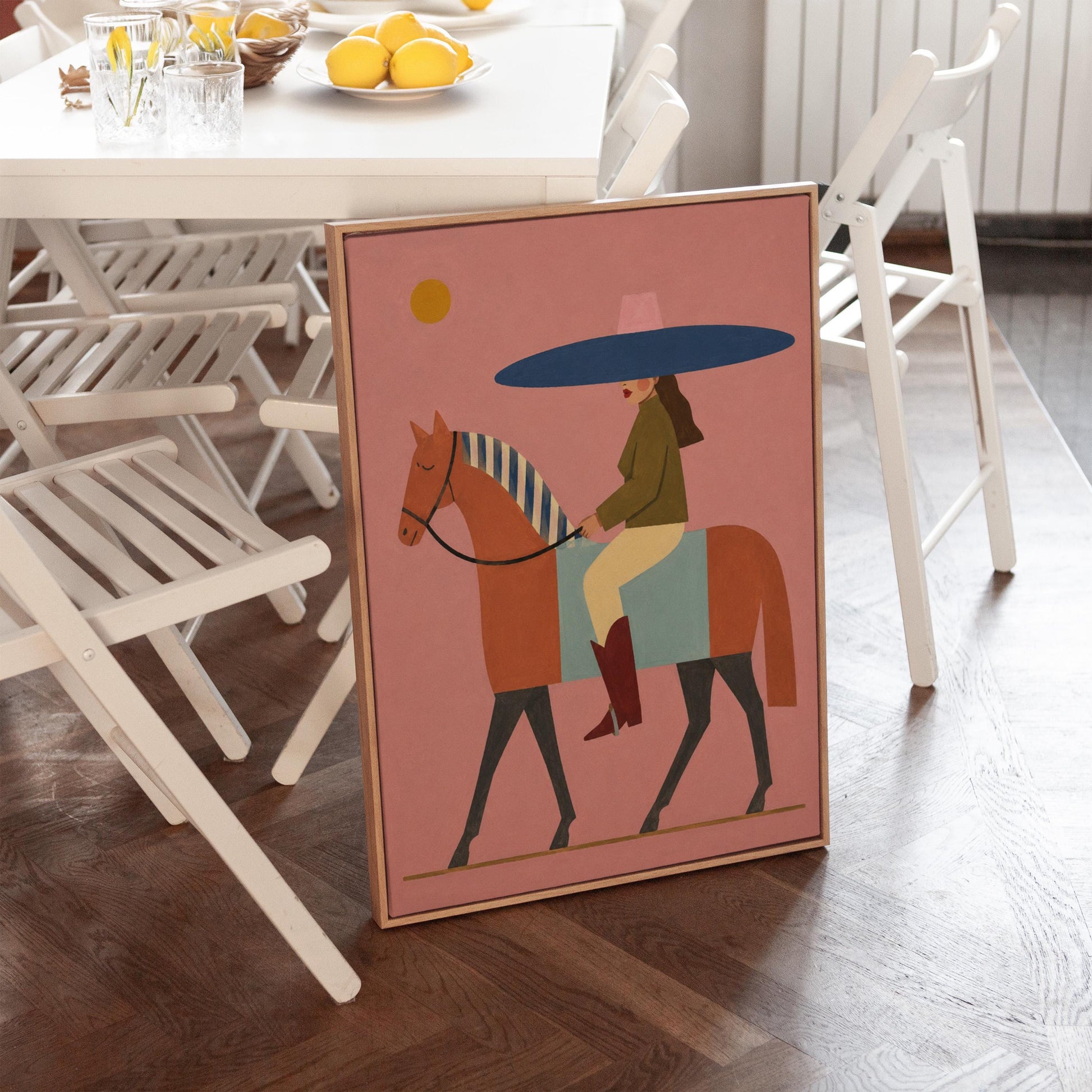 Woman in a wide navy hat riding a chestnut horse in profile on coral pink, canvas print hanging in a calm, modern living space