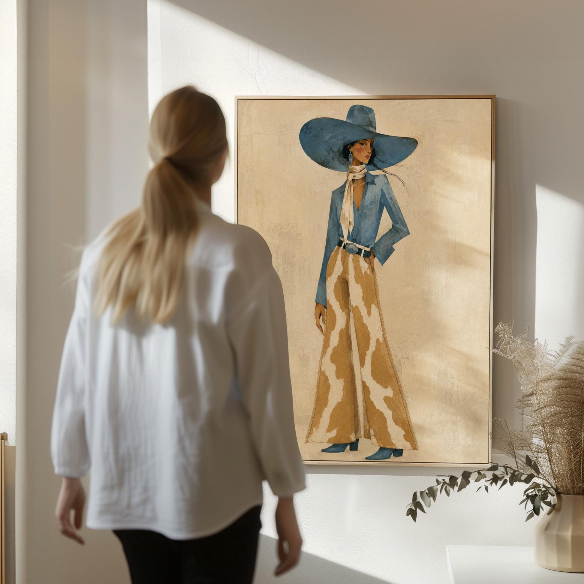 Full-figure cowgirl in a blue hat, denim shirt and cow-print flared pants on cream, canvas wall art styled against a soft white wall