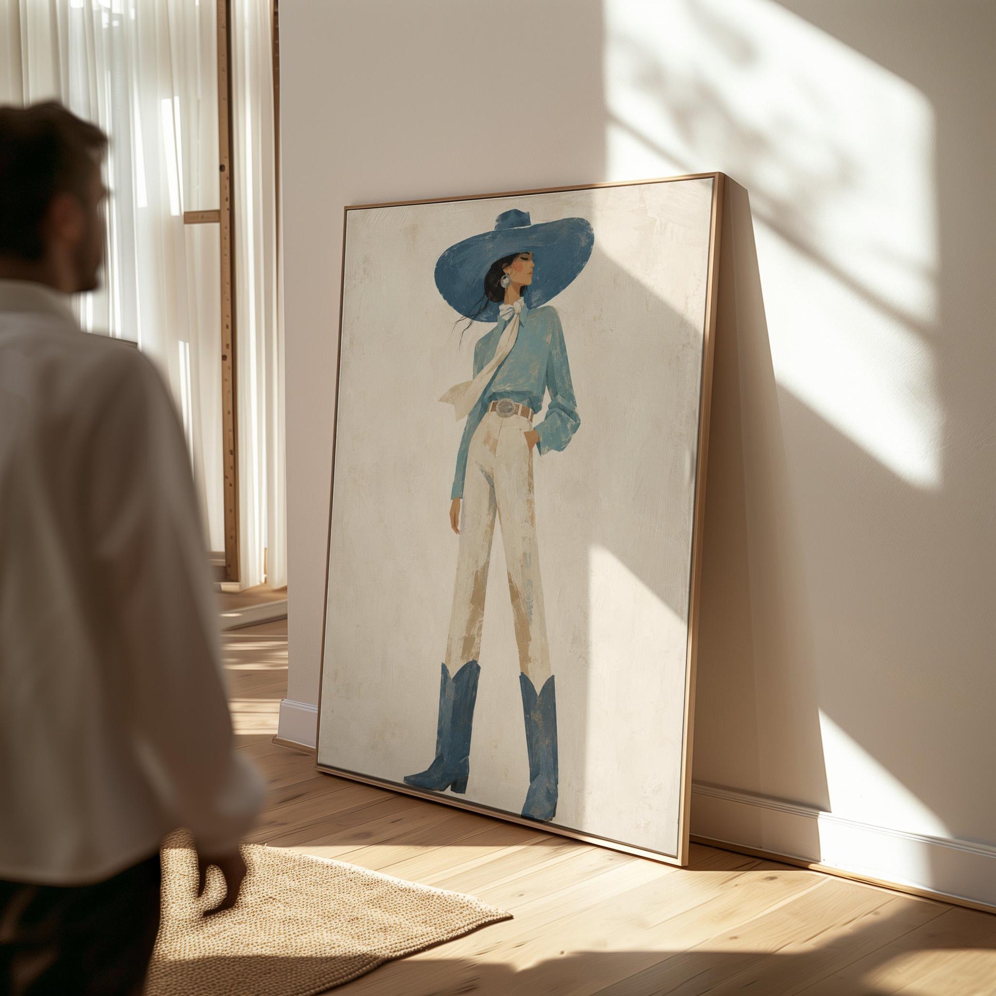 Full-figure cowgirl in a wide teal hat, blouse and boots with cream trousers, canvas wall art presented in a light, minimal room