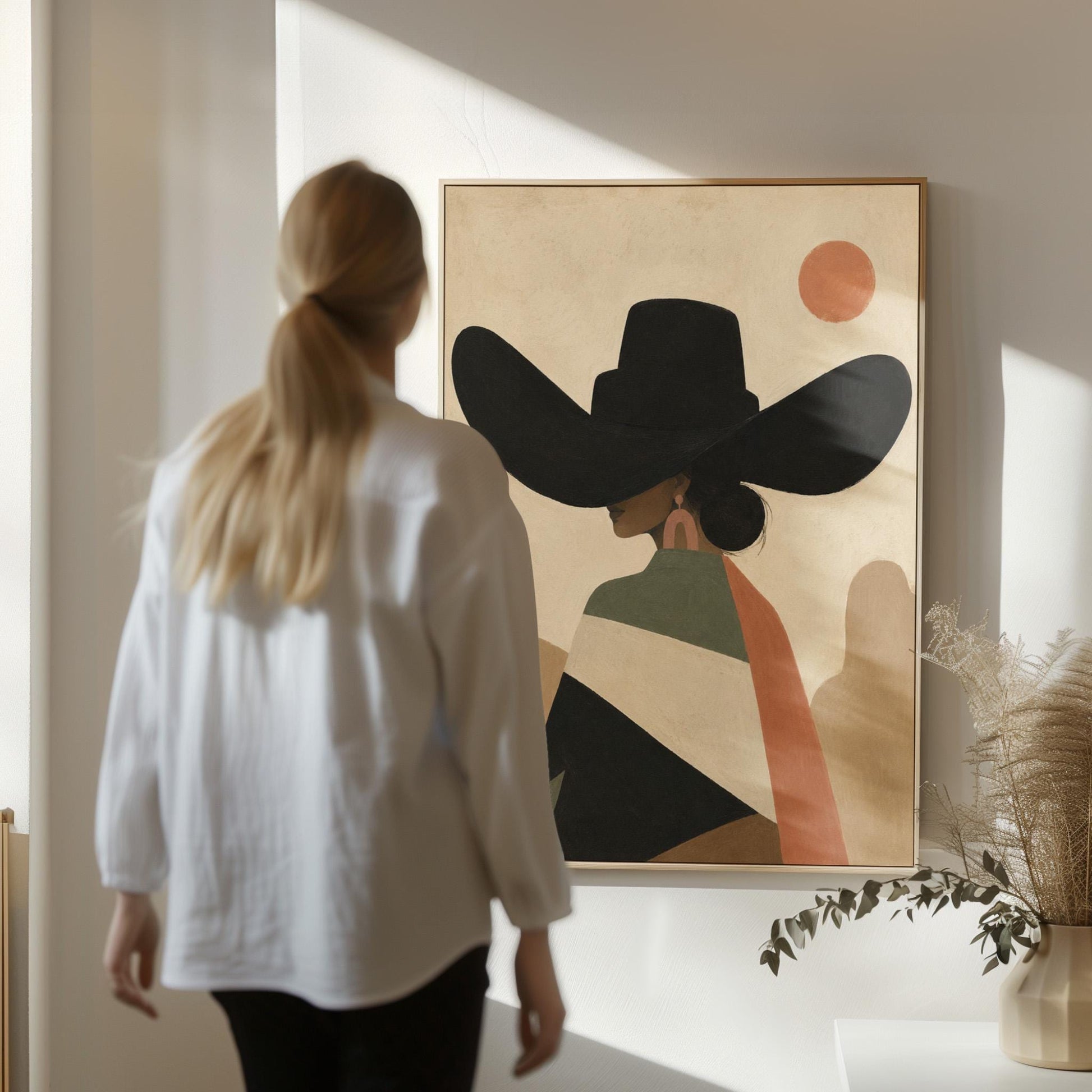 Cowgirl seen from behind in a large black hat and serape under a desert sun, canvas print seen in a warm interior with natural light