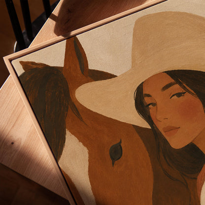 Cowgirl in a cream hat leaning cheek to cheek with a chestnut horse on warm tan, canvas print in a warm, minimally styled interior