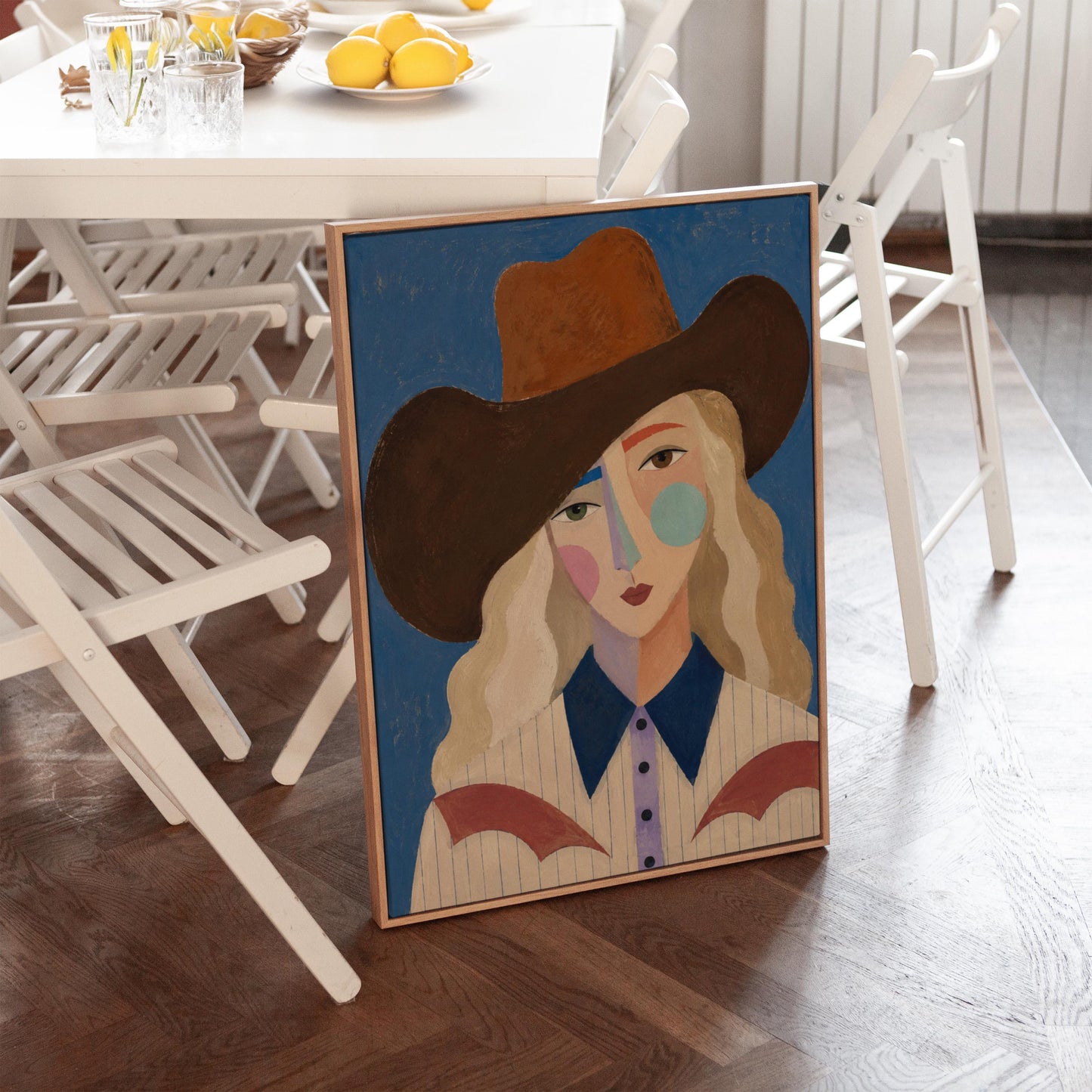 Blonde cowgirl in a rust hat with a cubist pastel face on deep blue, canvas print shown to scale in a furnished room