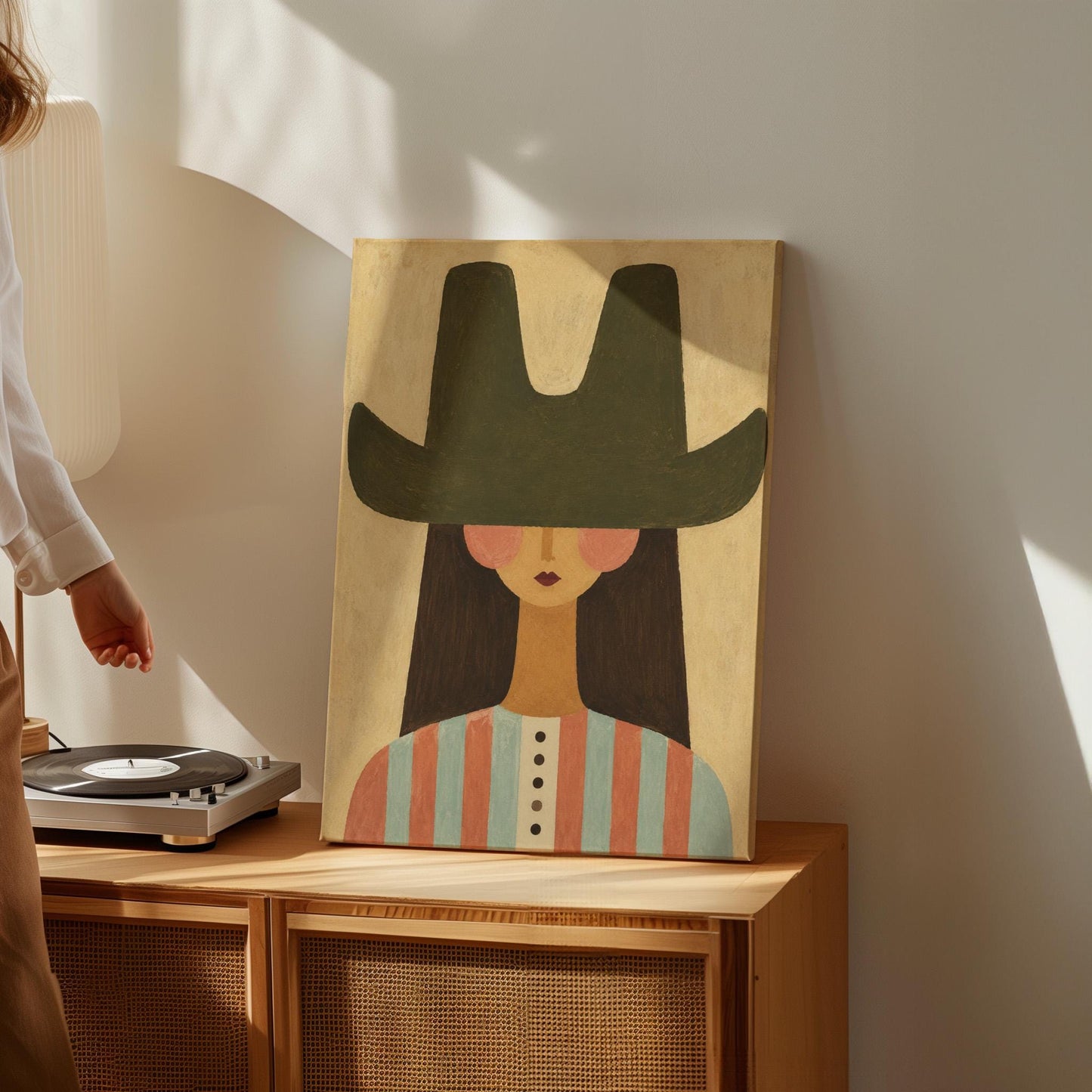 Folk cowgirl in a big green hat and striped shirt with long dark hair, canvas print seen in a warm interior with natural light