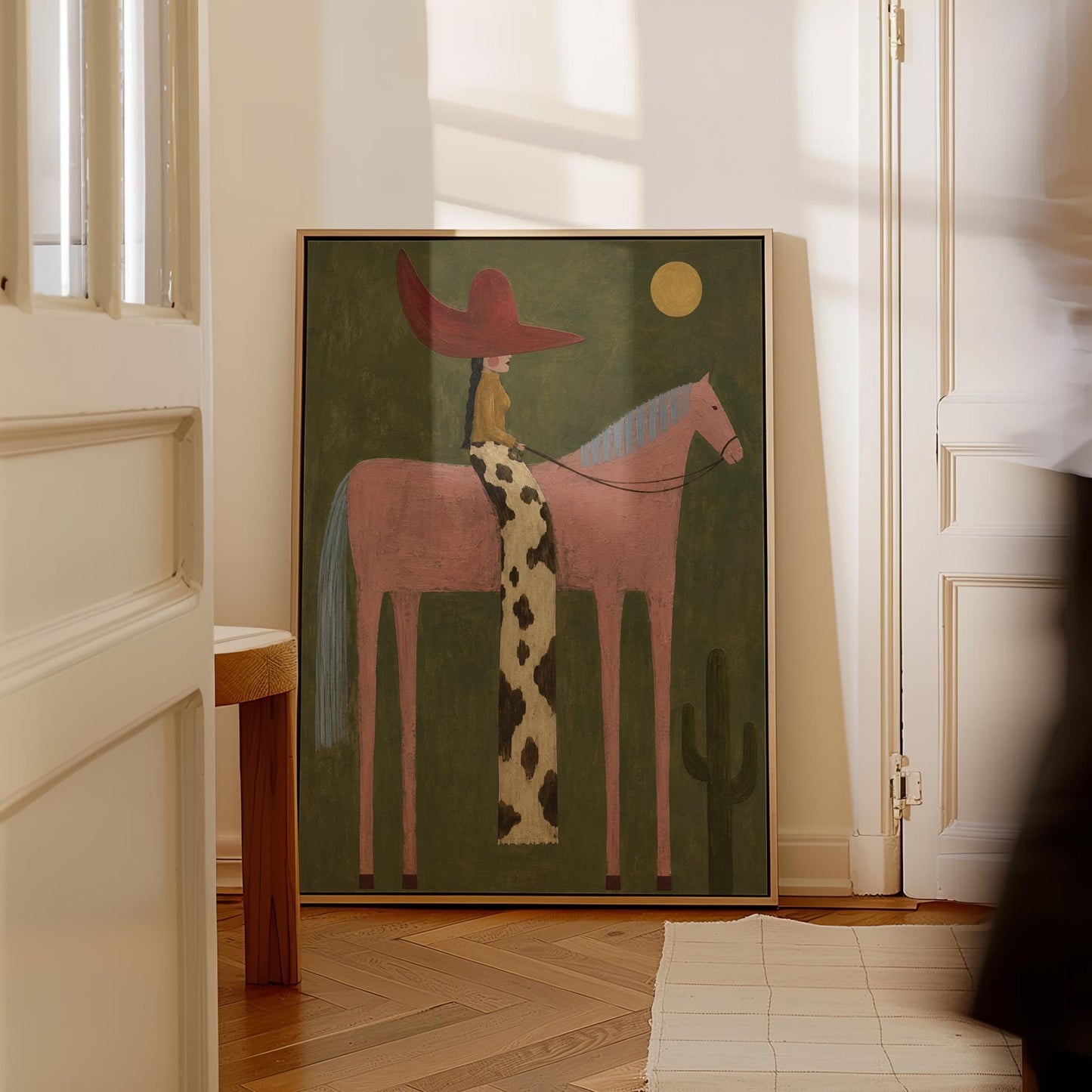 Cowgirl in a red hat riding a tall pink horse past a cactus under the moon, canvas wall art on a quiet wall in a considered interior