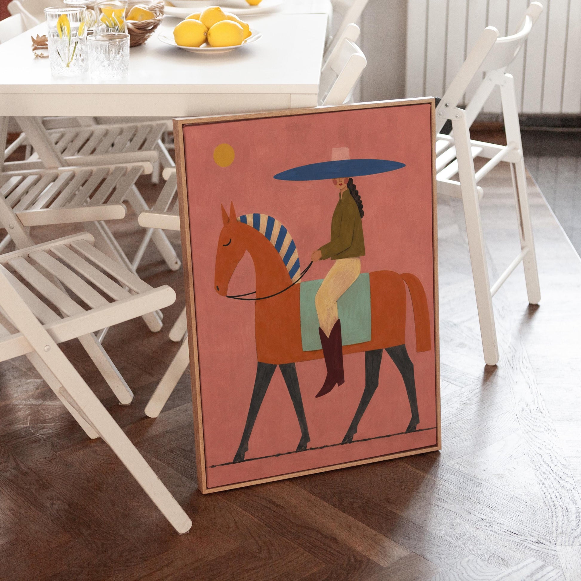 Cowgirl in a broad blue hat riding a rust red horse across a coral sky, canvas print on a quiet wall in a considered interior