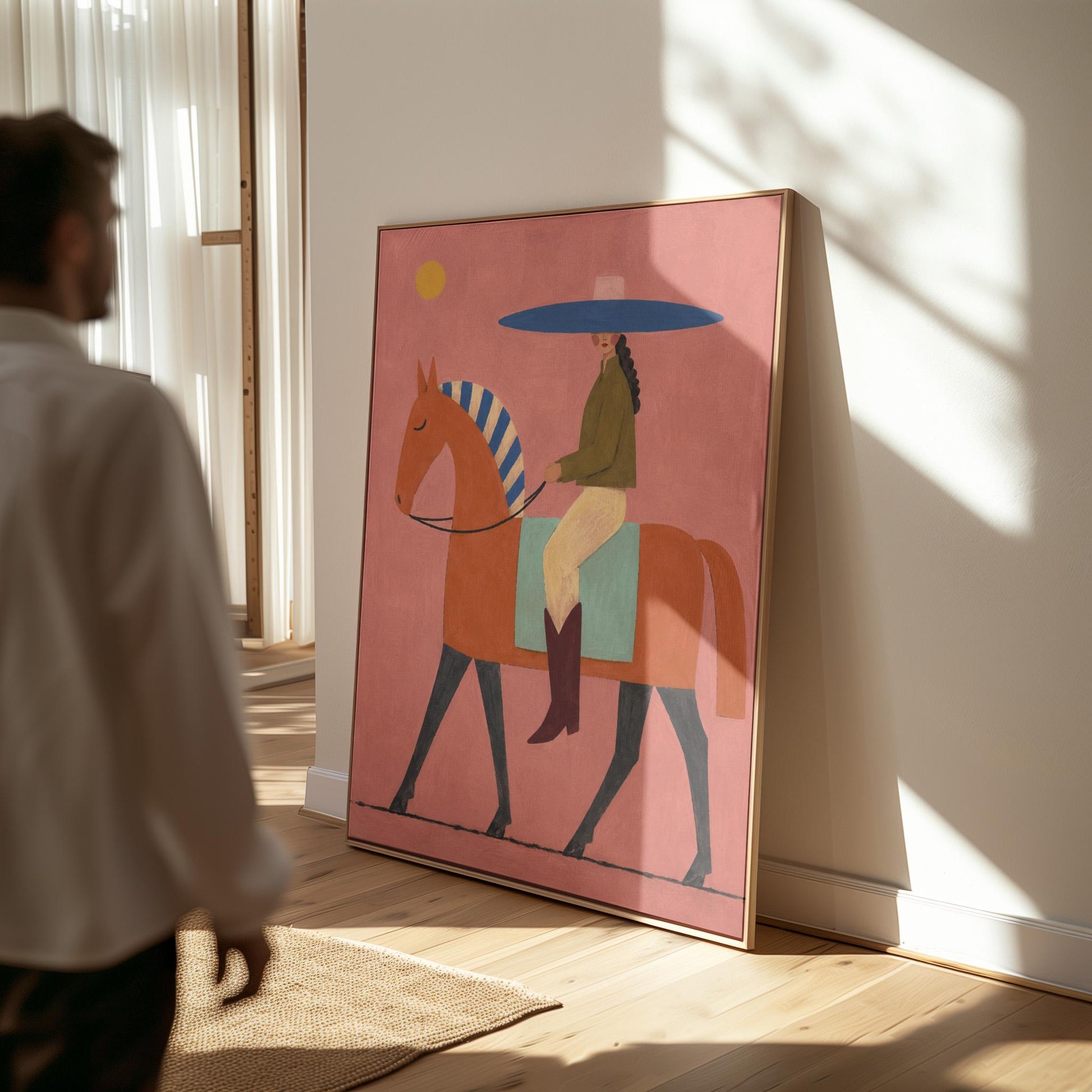 Cowgirl in a broad blue hat riding a rust red horse across a coral sky, canvas print shown to scale in a furnished room