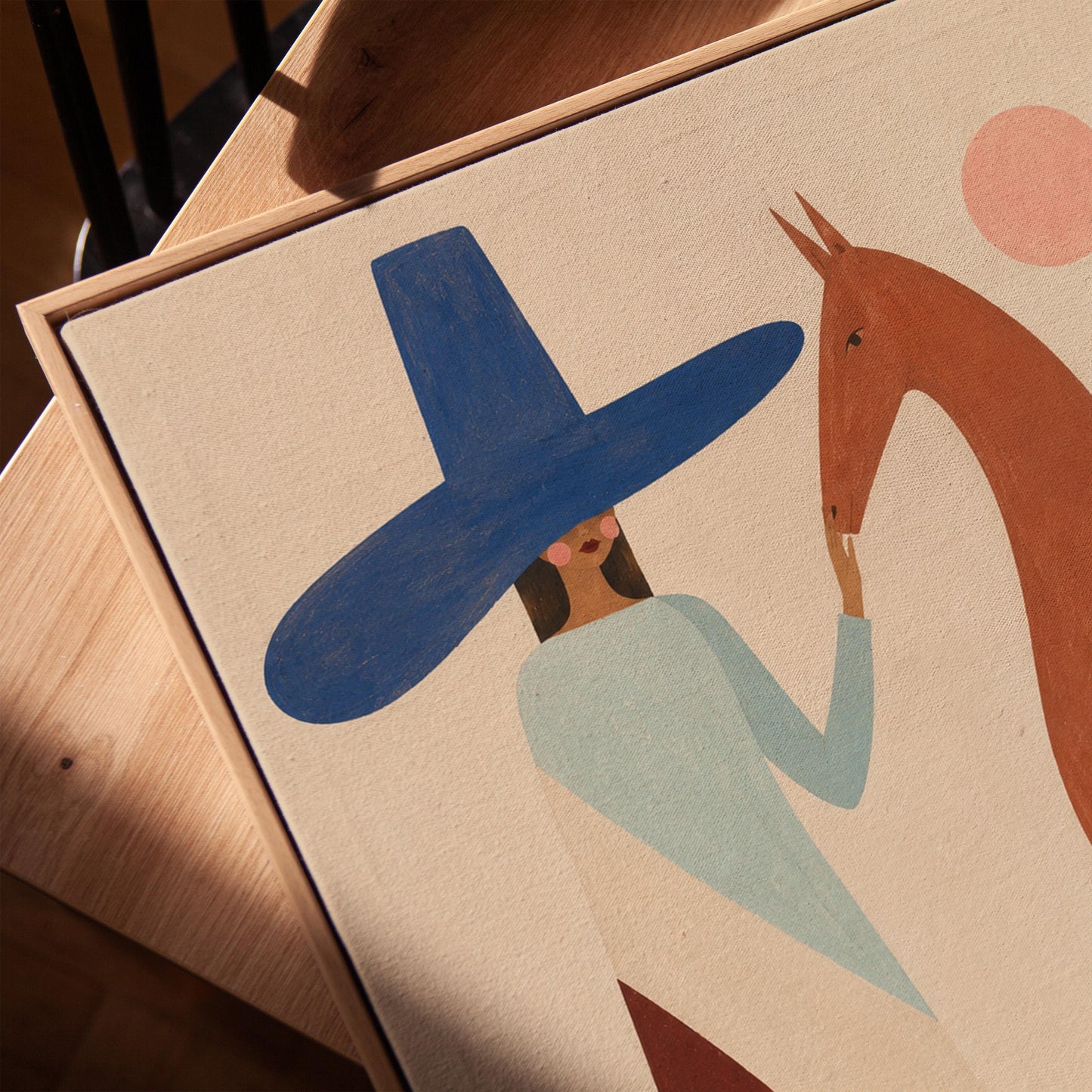 Woman in a tall blue hat reaching to a slim chestnut horse under a pink sun, canvas print in a warm, minimally styled interior