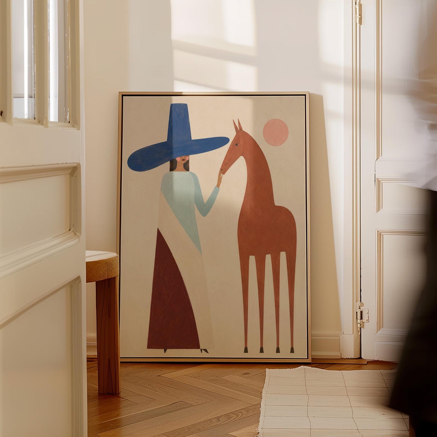 Woman in a tall blue hat reaching to a slim chestnut horse under a pink sun, canvas print presented in a light, minimal room