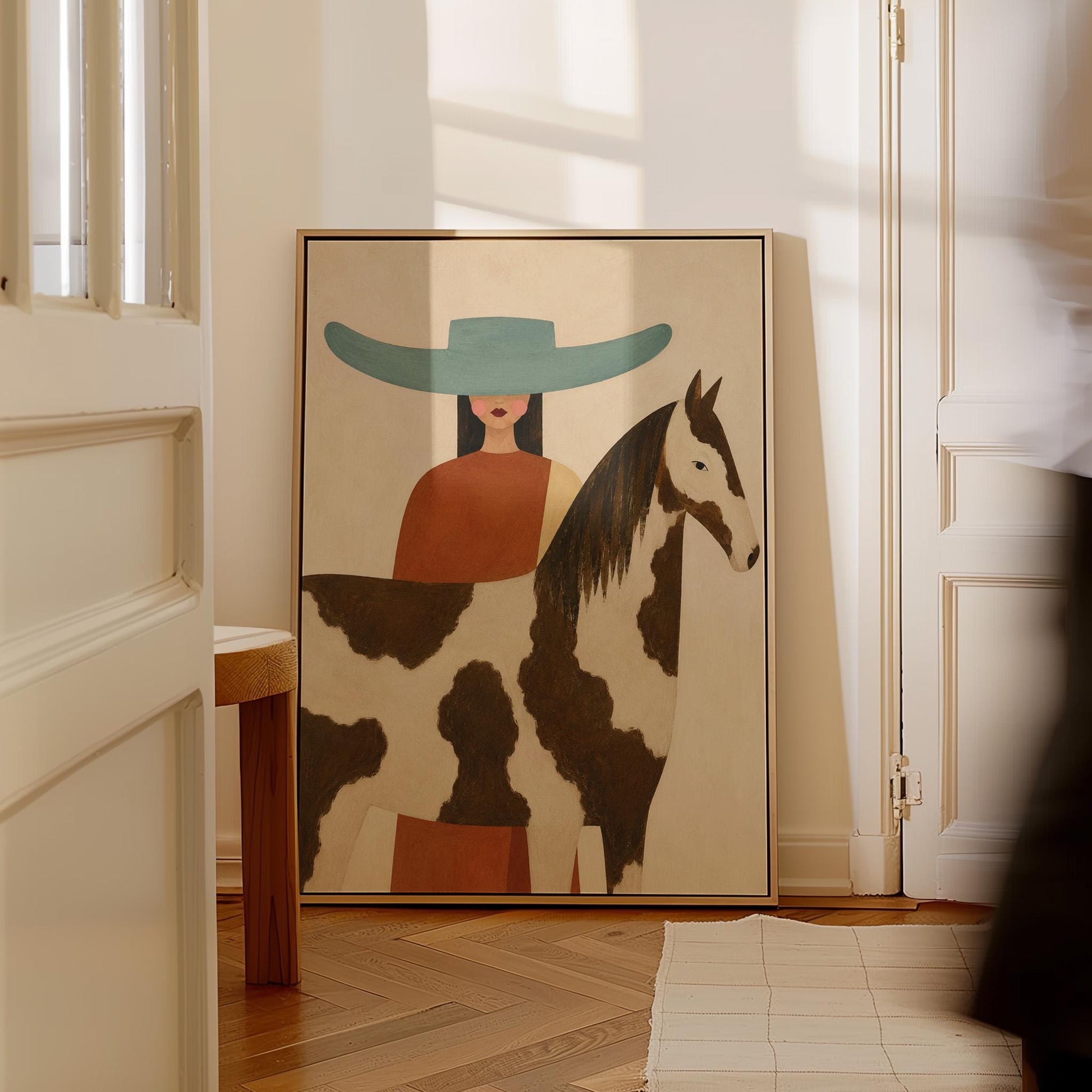 Woman in a teal hat beside a brown and white pinto horse in warm light, canvas print shown in a sunlit, contemporary room