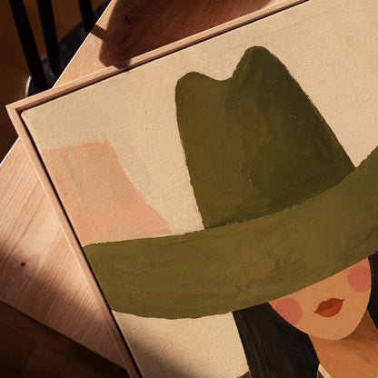 Faceless cowgirl portrait under a broad olive green hat, canvas print in a warm, minimally styled interior