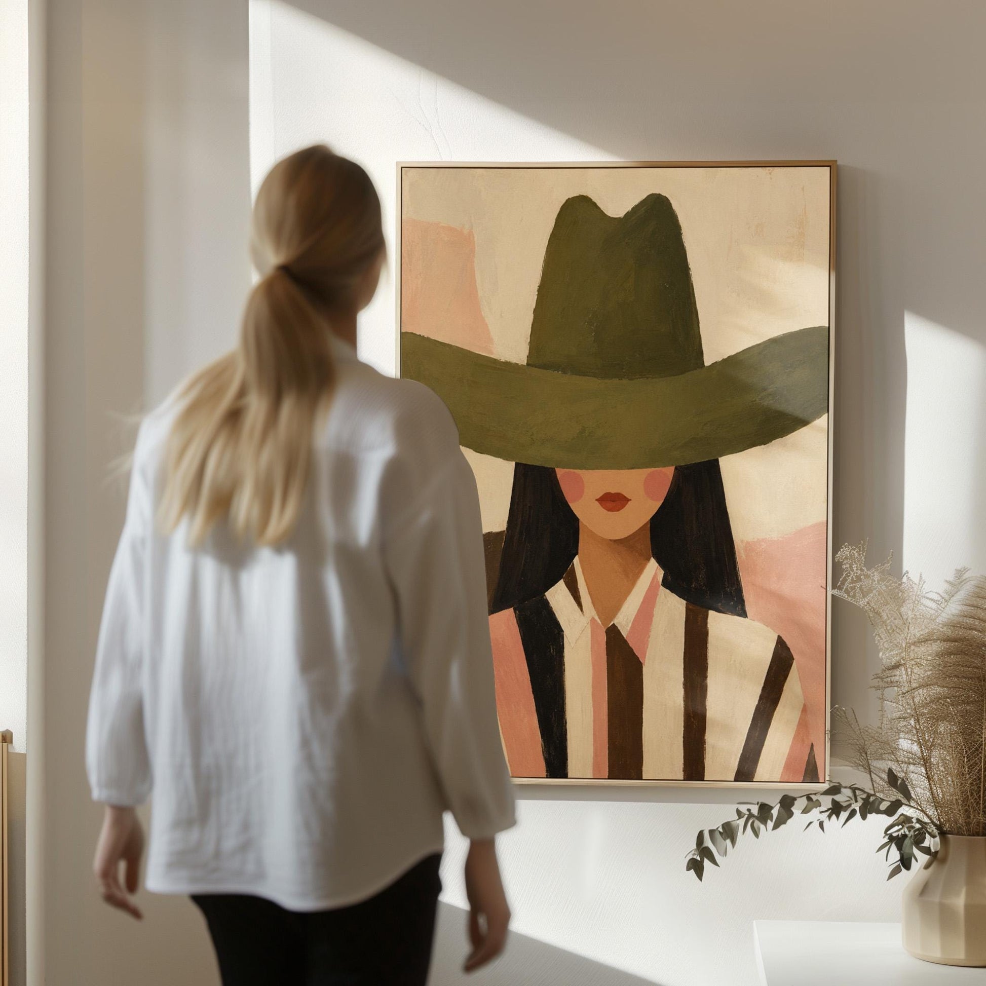 Faceless cowgirl portrait under a broad olive green hat, canvas wall art on a quiet wall in a considered interior