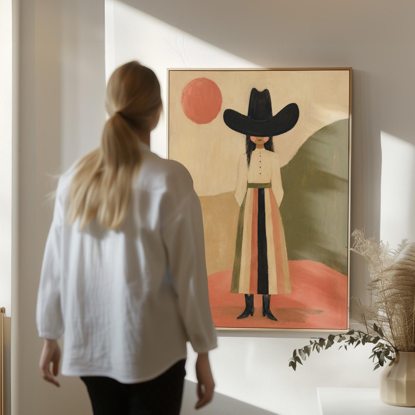 Figure in black cowboy hat standing between coral desert hills, canvas wall art hanging in a calm, modern living space