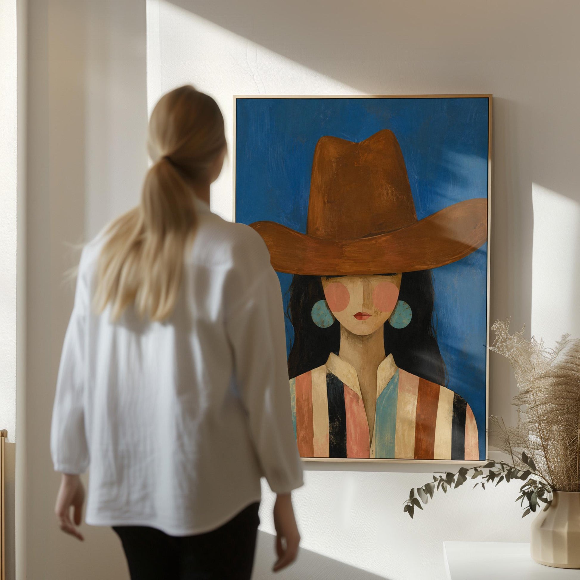 Cowgirl in a brown hat and turquoise earrings on cobalt blue, canvas wall art seen in a warm interior with natural light