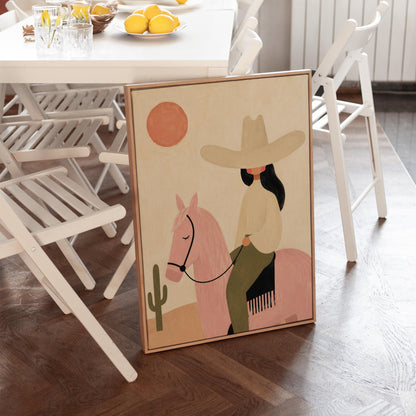 Cowgirl in a pale hat riding a soft pink horse past a desert cactus, canvas print seen in a warm interior with natural light