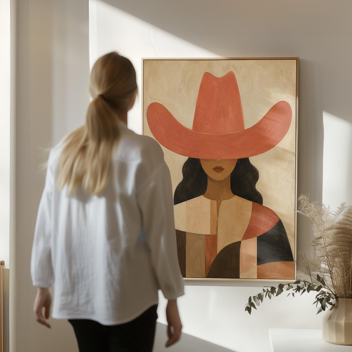 Cowgirl in a broad terracotta hat and patchwork western shirt, canvas print hanging in a calm, modern living space