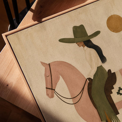 Cowgirl on a dusty pink horse beside a tall saguaro cactus, canvas print in a warm, minimally styled interior