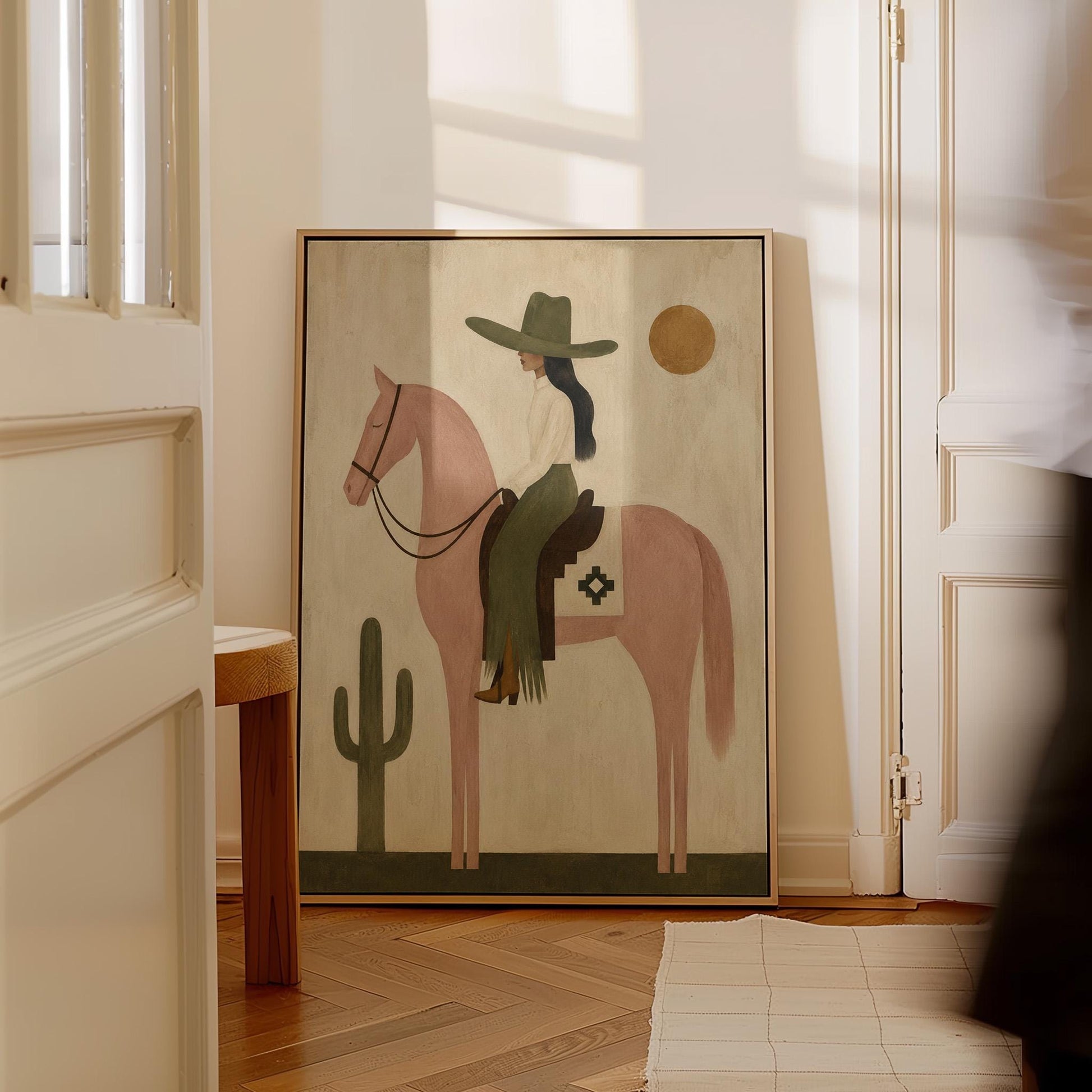 Cowgirl on a dusty pink horse beside a tall saguaro cactus, canvas print shown in a sunlit, contemporary room