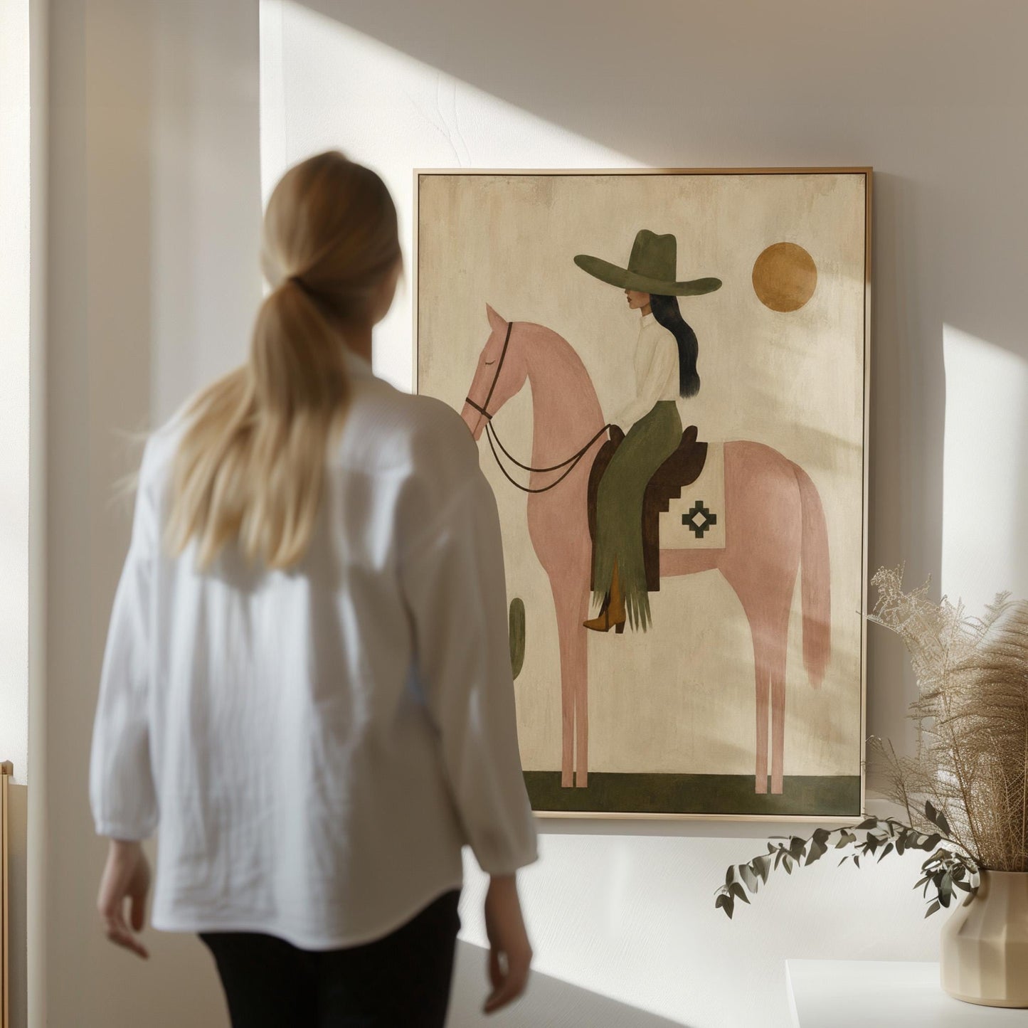 Cowgirl on a dusty pink horse beside a tall saguaro cactus, canvas wall art hanging in a calm, modern living space