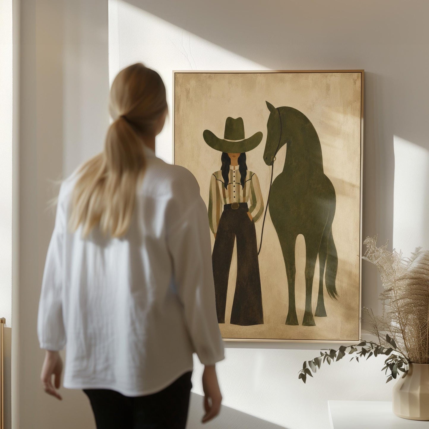 Cowgirl in wide trousers leading a flat olive green horse, canvas print presented in a light, minimal room