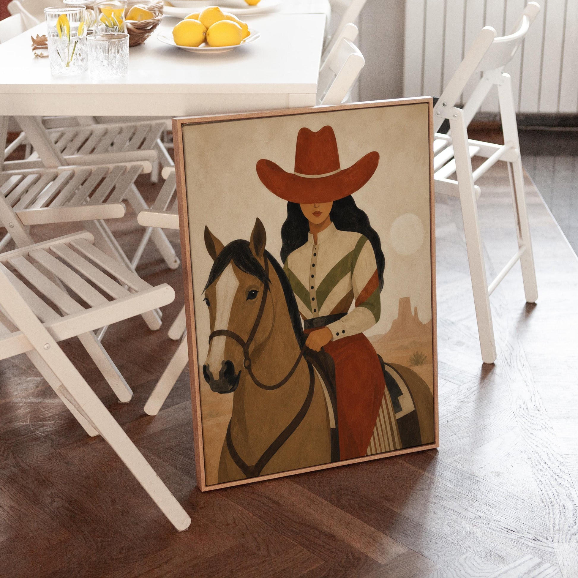 Cowgirl in a red hat riding a bay horse across an ochre desert, canvas print displayed on a neutral wall in a styled interior